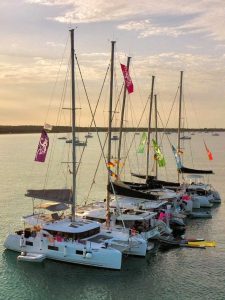 Colorful sailing yachts moored at sunset on the calm sea, with vibrant flags flying from their masts, creating a lively and picturesque maritime scene.